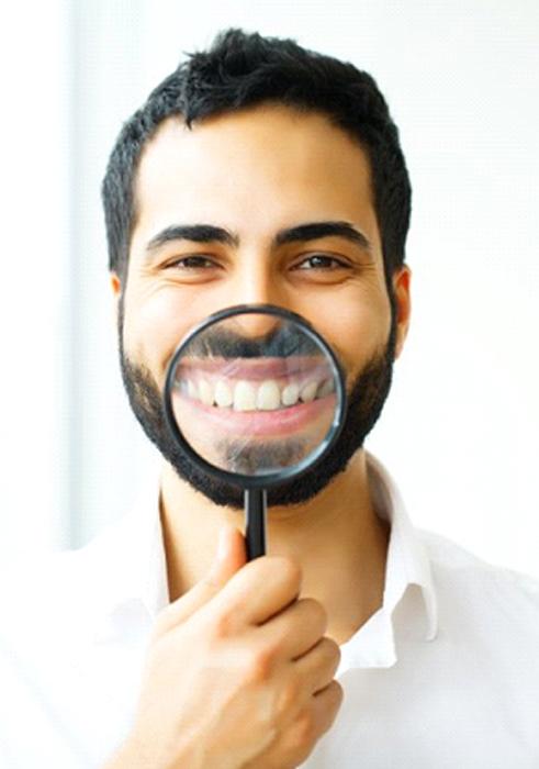 Man with porcelain veneers in Charleston showing off his smile with a magnifying glass