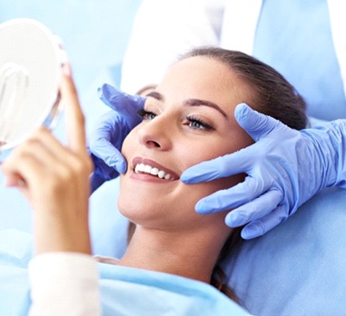 Dental patient admiring her new smile in a mirror after porcelain veneer placement