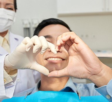 a dentist and a patient framing the patients smile by making a heart with their hands